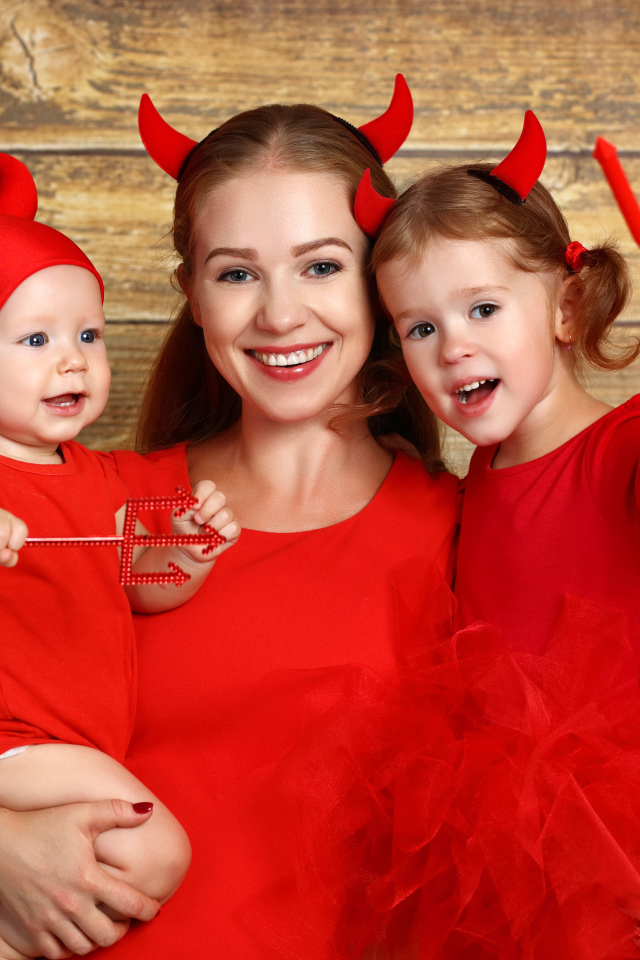 Женщина с двумя детьми в красных костюмах на Хэллоуин