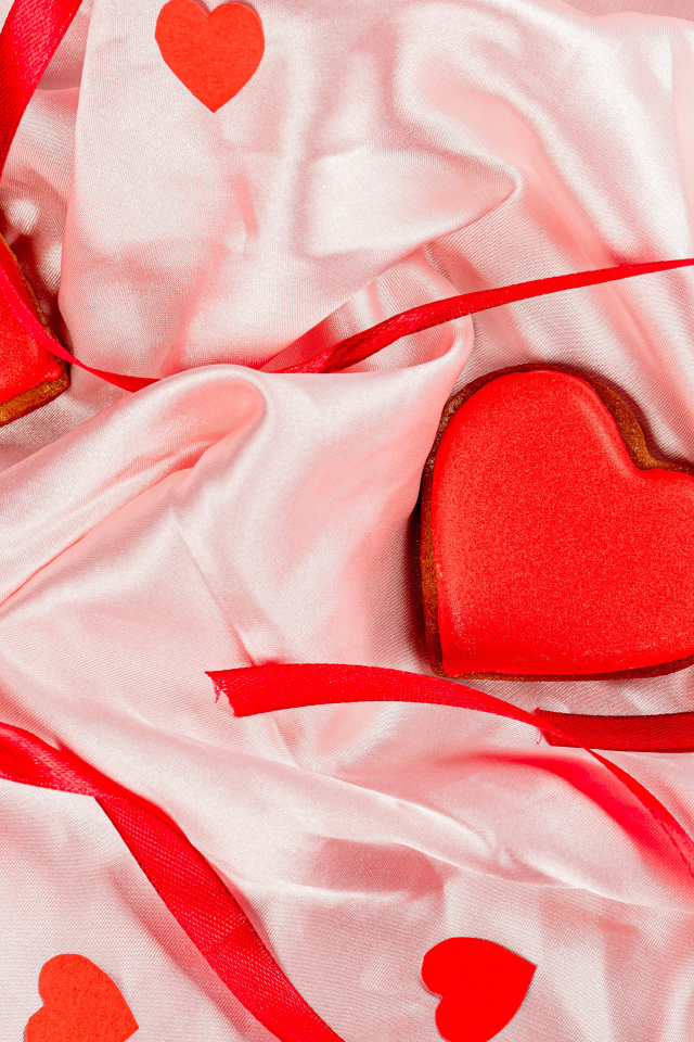 Два красных сердечка с ленточкой на розовой ткани на день влюбленных