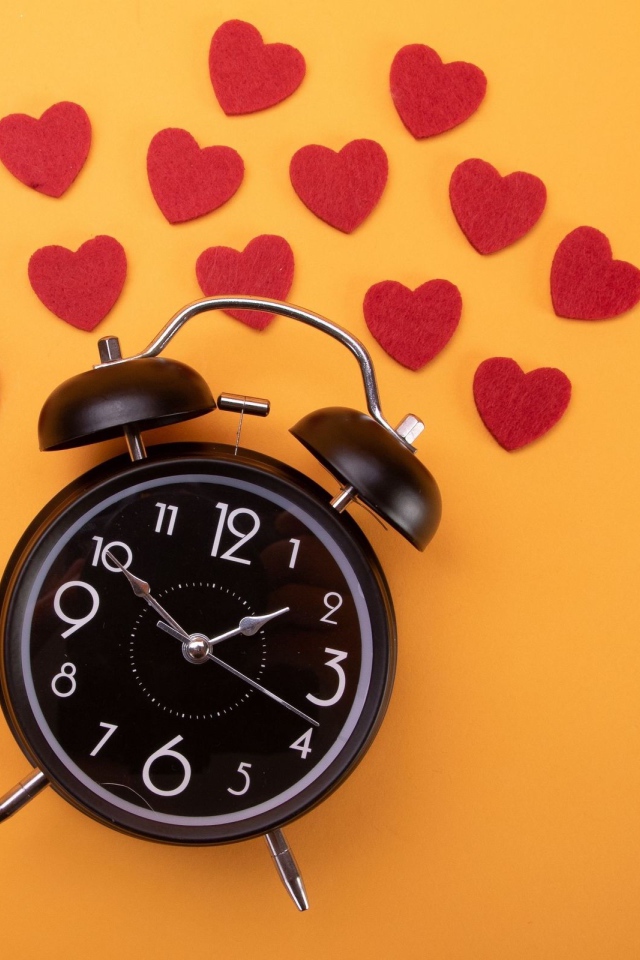 Черный будильник с сердечками на оранжевом фоне
