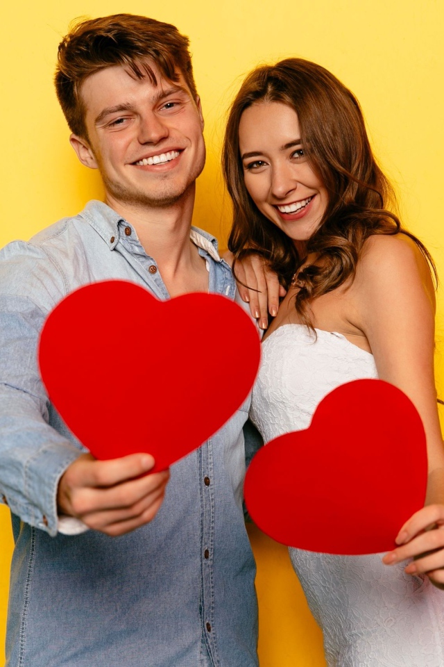 Влюбленная пара на желтом фоне с бумажными сердечками в руках 