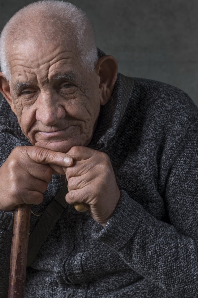 Пожилой мужчина в теплом свитере на сером фоне 