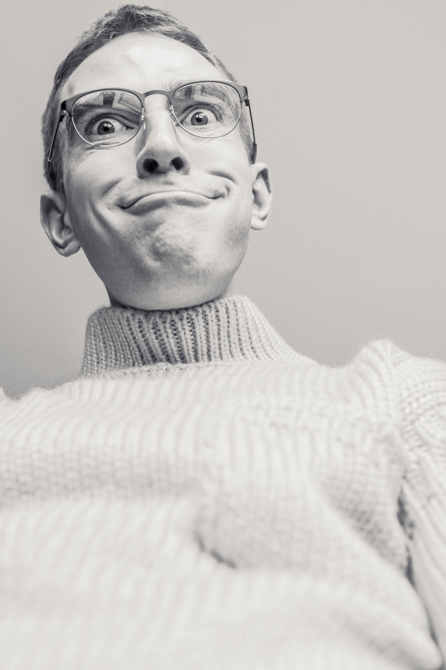 Мужчина в очках корчит лицо на сером фоне