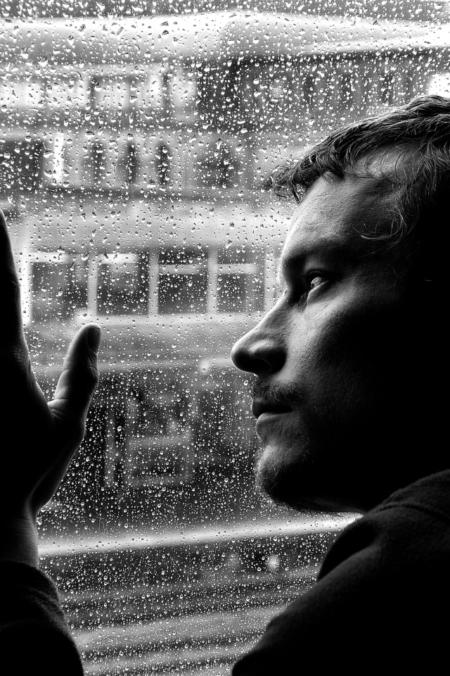 Грустный мужчина стоит у мокрого окна 