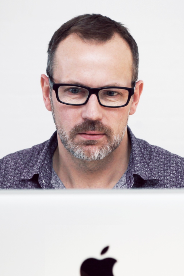 Серьезный мужчина в очках сидит за макбуком