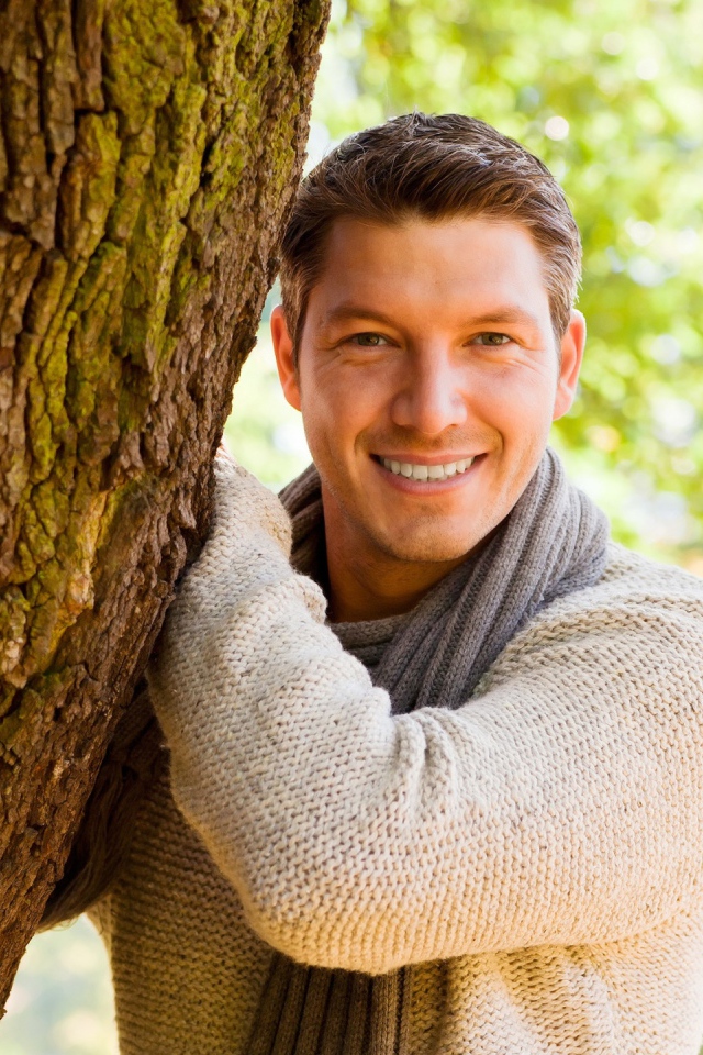 Улыбающийся мужчина стоит у дерева 