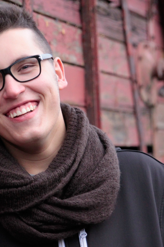 Улыбающийся мужчина в очках у стены 