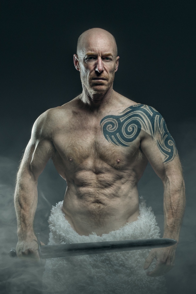 Сильный мужчина с мечом с татуировками на теле 