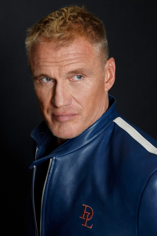 Актер Дольф Лундгрен в куртке на фоне  серой стены