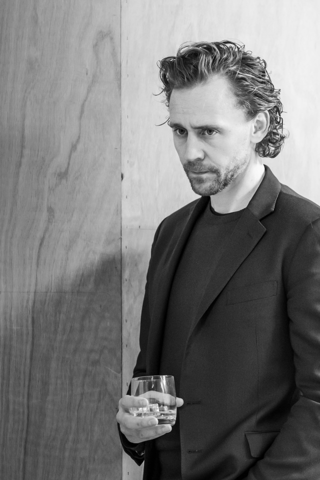 Актер Том Хиддлстон с бокалом в руке на фоне стены