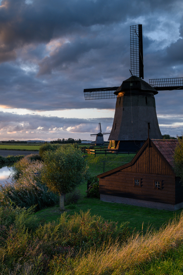 Большая ветряная мельница у реки на закате