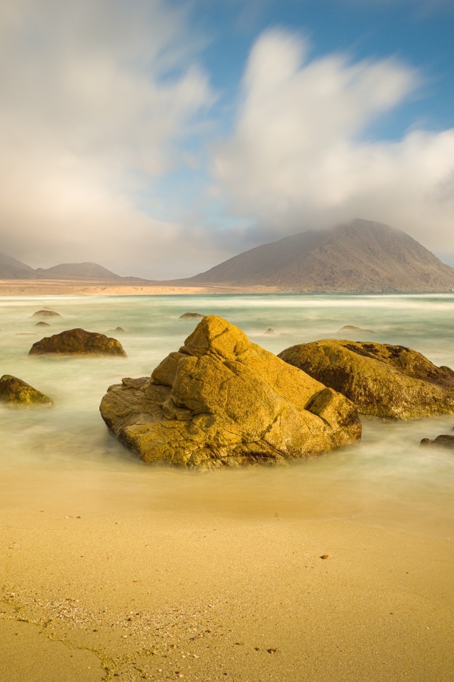 Большие камни лежат в воде на песке 