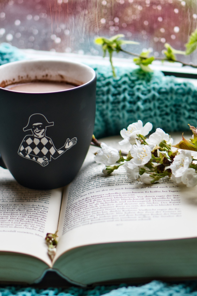 Цветущая ветка вишни на столе с книгой и чашкой кофе