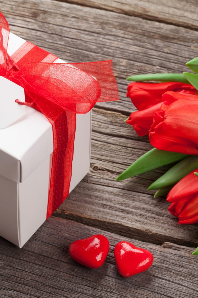 Красные тюльпаны с большим подарком на деревянном столе 