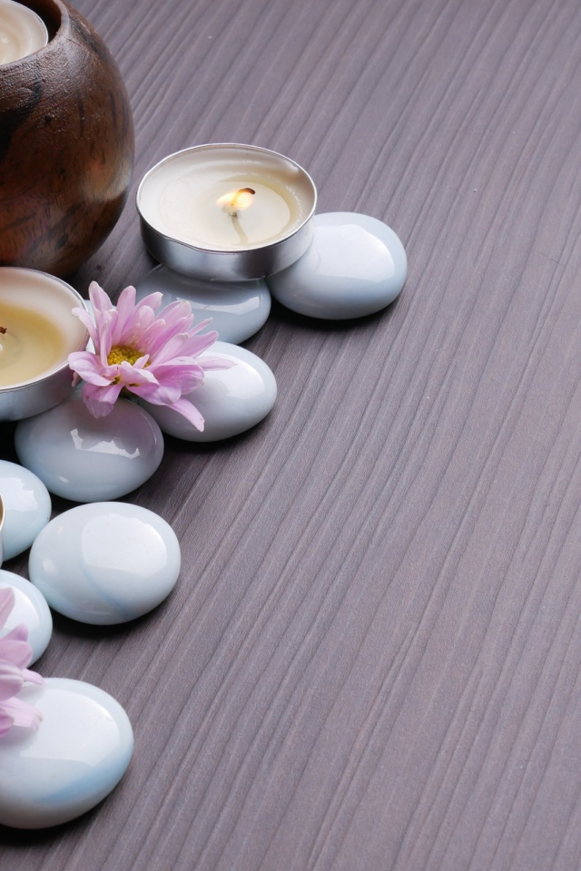 Камни с хризантемами и зажженными свечами на столе 