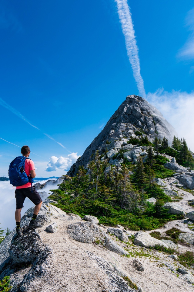Мужчина подымается на вершина горы под голубым небом 