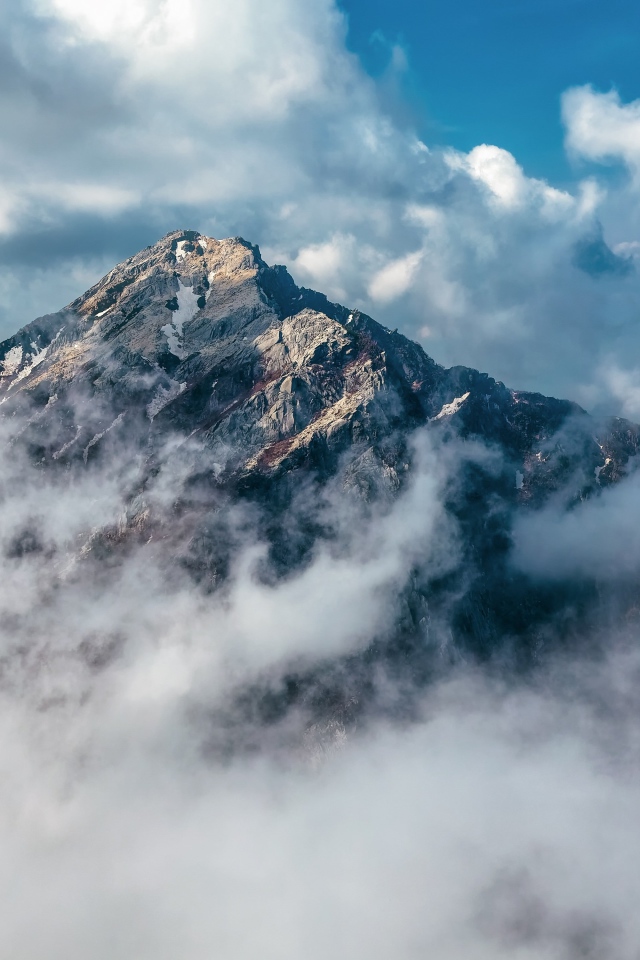 Большая высокая гора в густых белых облаках