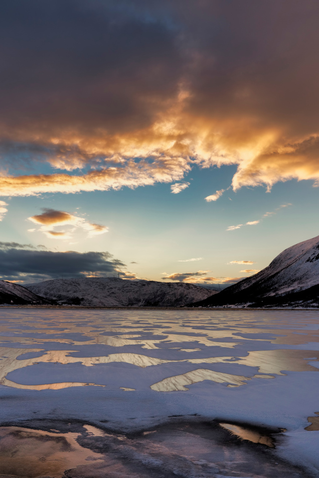 Покрытое льдом озеро у гор на закате солнца 
