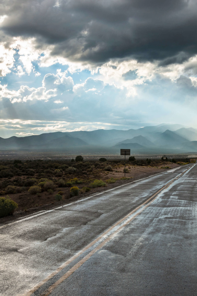 Мокрая дорога в лучах солнца под пасмурным небом 