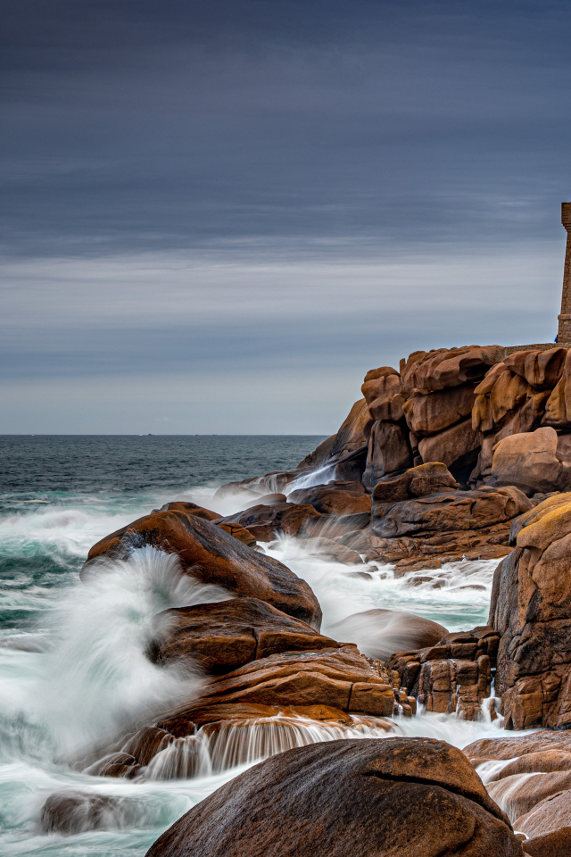Старая башня маяка на каменном берегу у моря 