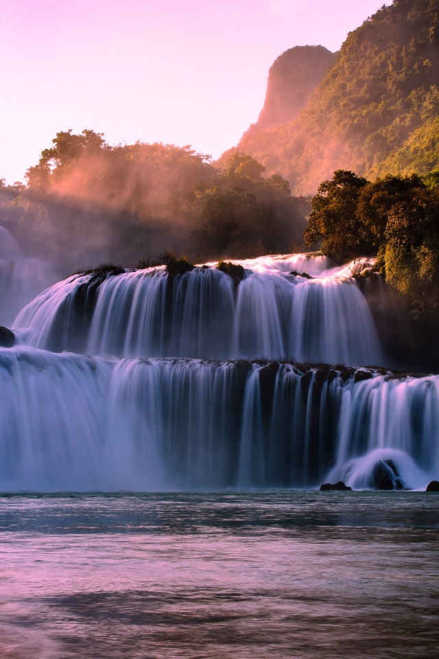 Каскадный водопад стекает по камням в лучах солнца 