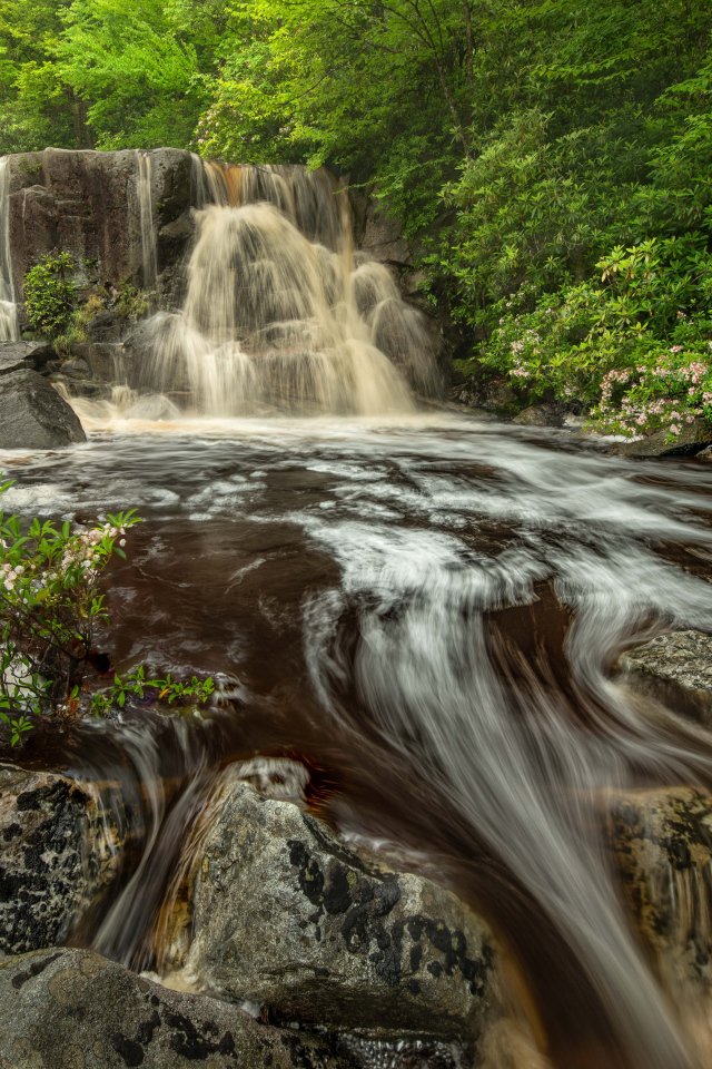 Быстрая холодная вода водопада стекает по большим камням