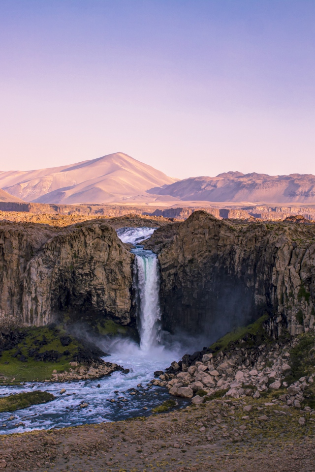 Водопад стекает по каменному склону горы на рассвете 