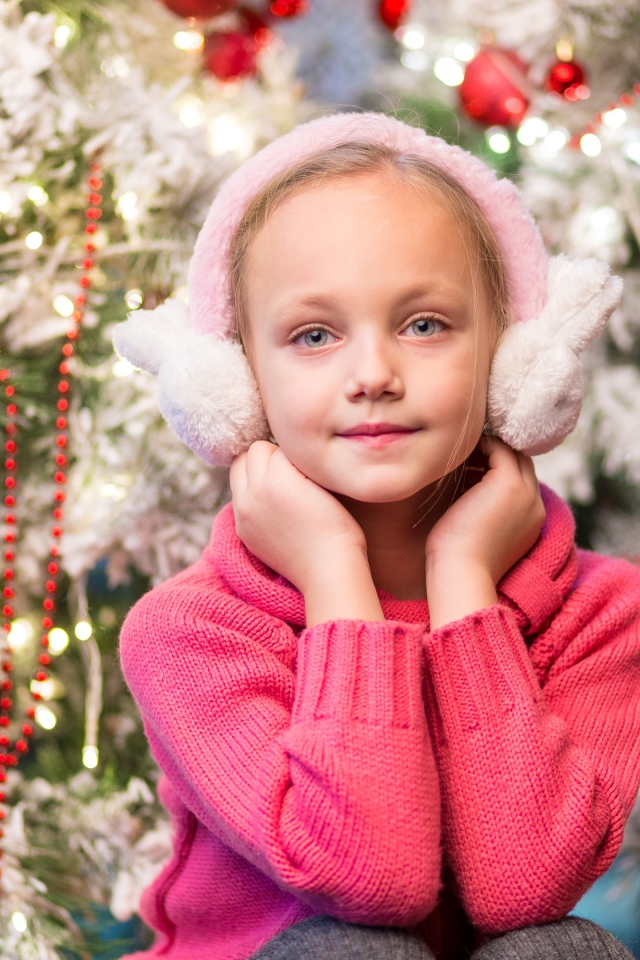 Девочка в розовых наушниках сидит у ели