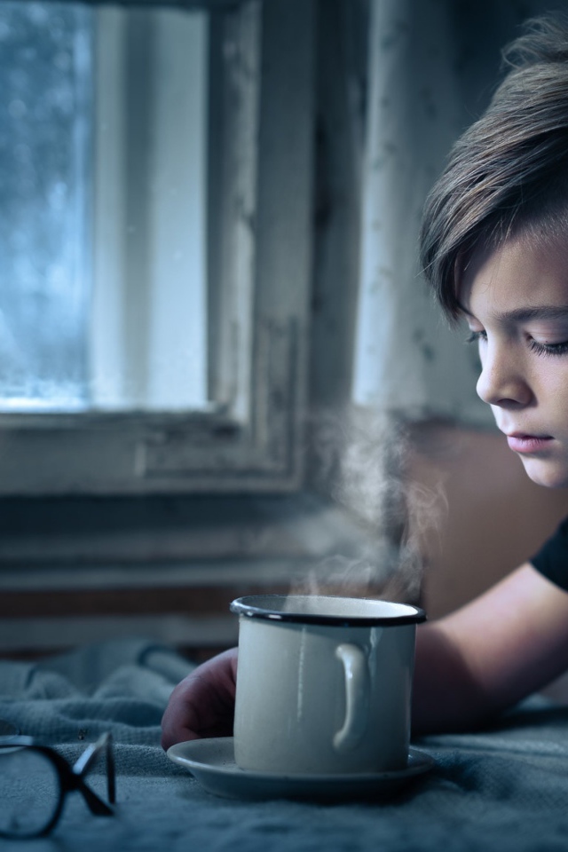 Маленький мальчик сидит за столом при свете свечи 