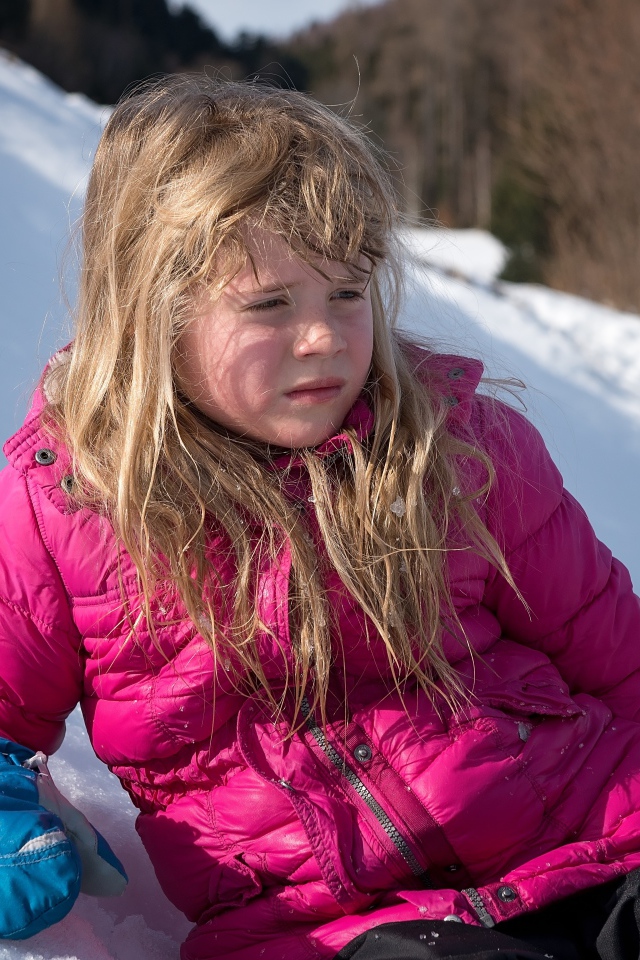 Маленькая девочка лежит на заснеженной горке 