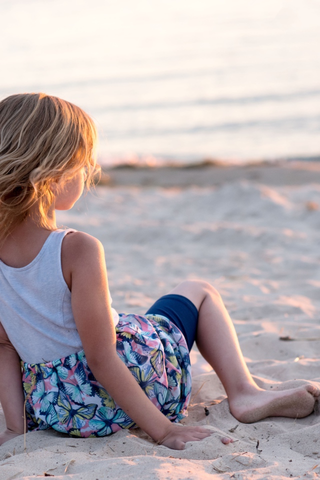 Маленькая девочка лежит на песке на закате 