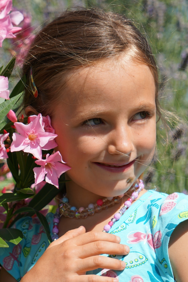 Маленькая девочка стоит у растения с розовыми цветами 