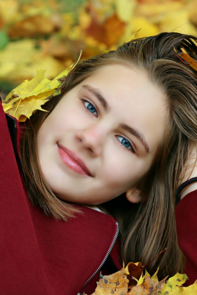 Красивая голубоглазая девочка лежит на опавшей листве