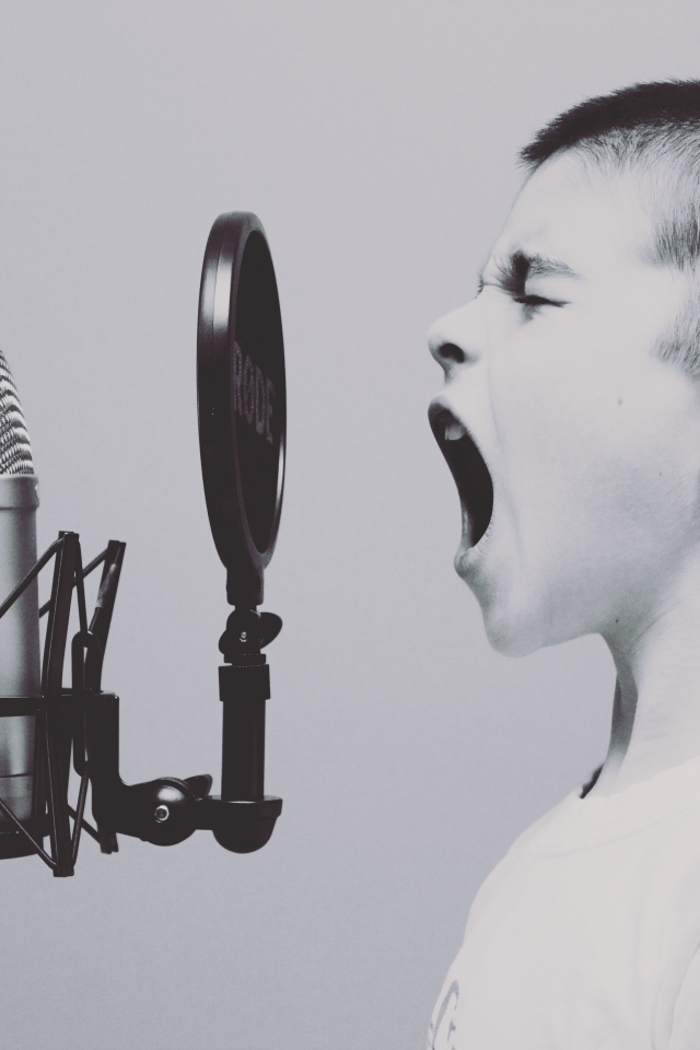 Мальчик кричит в студийный микрофон на сером фоне 