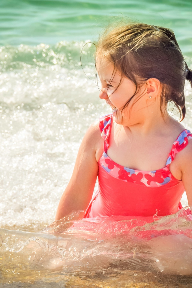 Веселая маленькая девочка в купальнике сидит в воде 