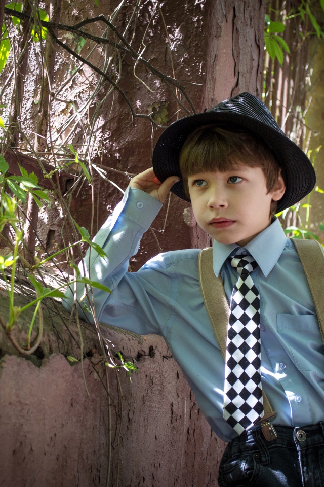 Красивый мальчик в шляпе стоит у забора 