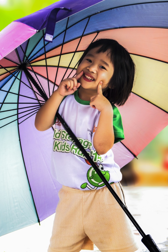 Маленькая девочка азиатка под большим разноцветным зонтом 