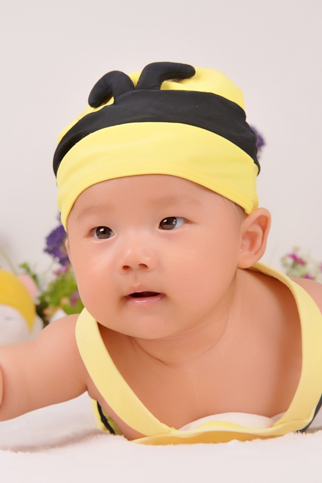 Маленький мальчик в шапке пчелы на сером фоне 