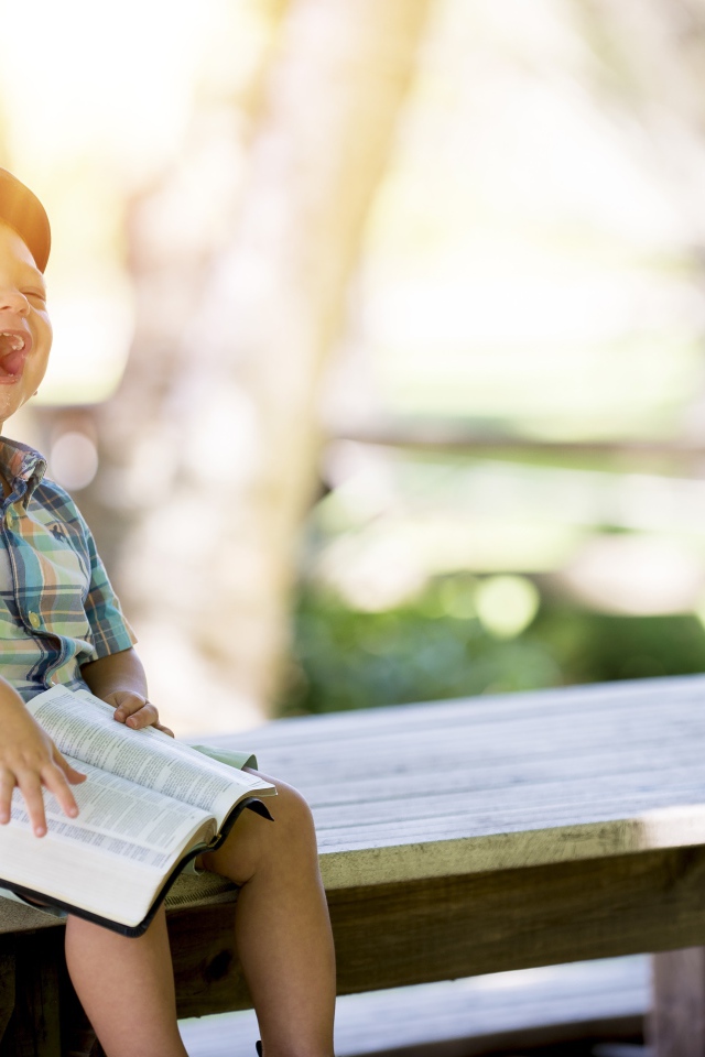 Маленький мальчик смеется на лавке с книгой