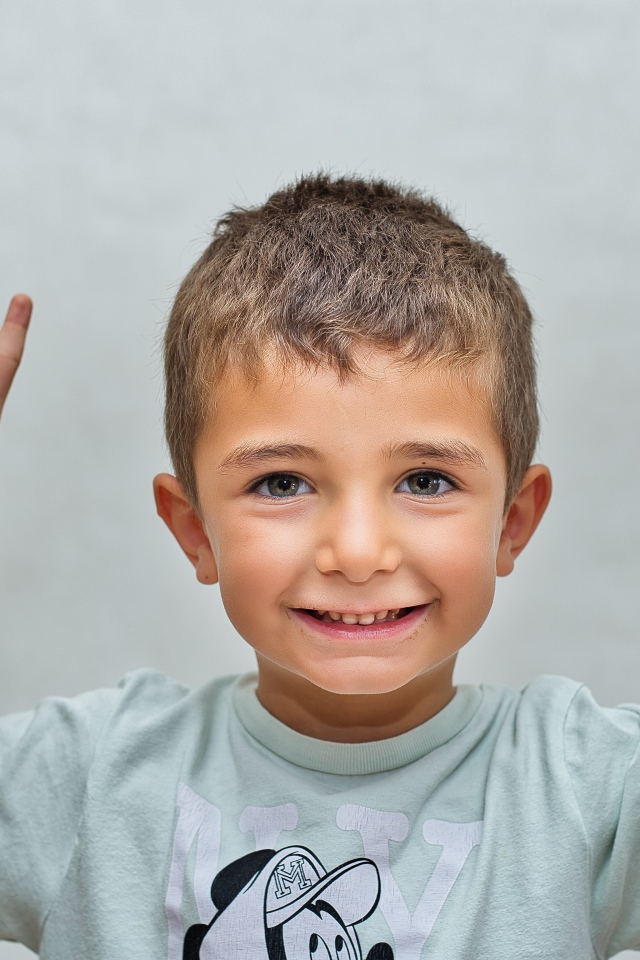 Маленький мальчик поднял руки вверх на сером фоне