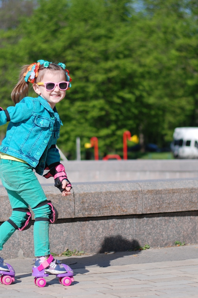 Маленькая веселая девочка катается на роликах
