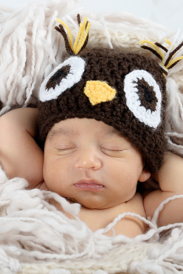 Маленький ребенок  в вязаной шапке спит на кровати 