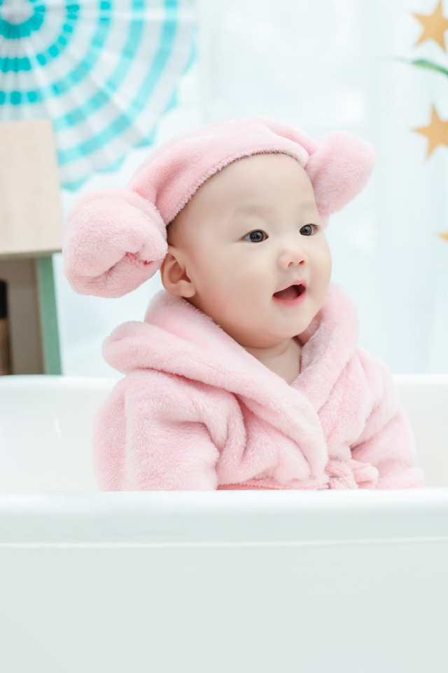 Маленький ребенок в розовом халате сидит в белой ванной