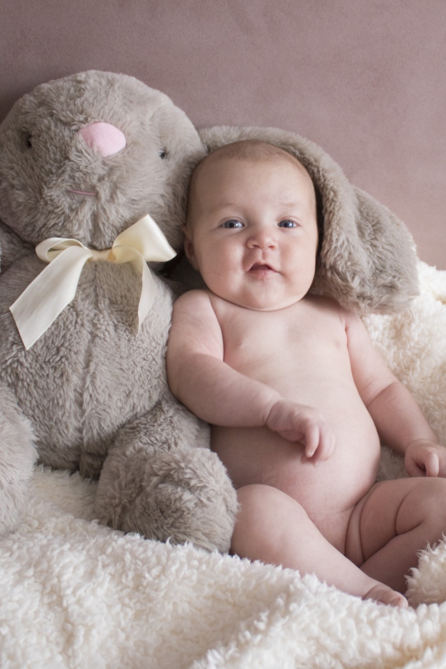 Маленький ребенок с игрушкой сидит у стены