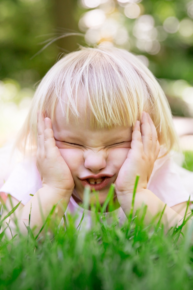 Маленькая смешная девочка лежит на зеленой траве 
