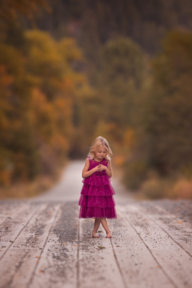 Маленькая девочка в платье стоит на мосту 