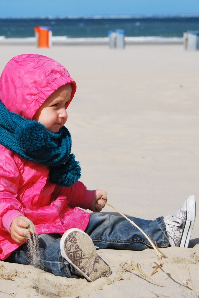 Маленькая девочка в розовой куртке на песке
