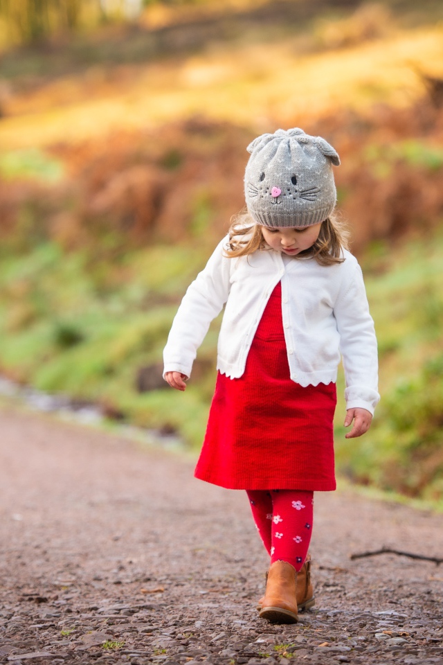 Маленькая девочка в красном платье идет по дороге 