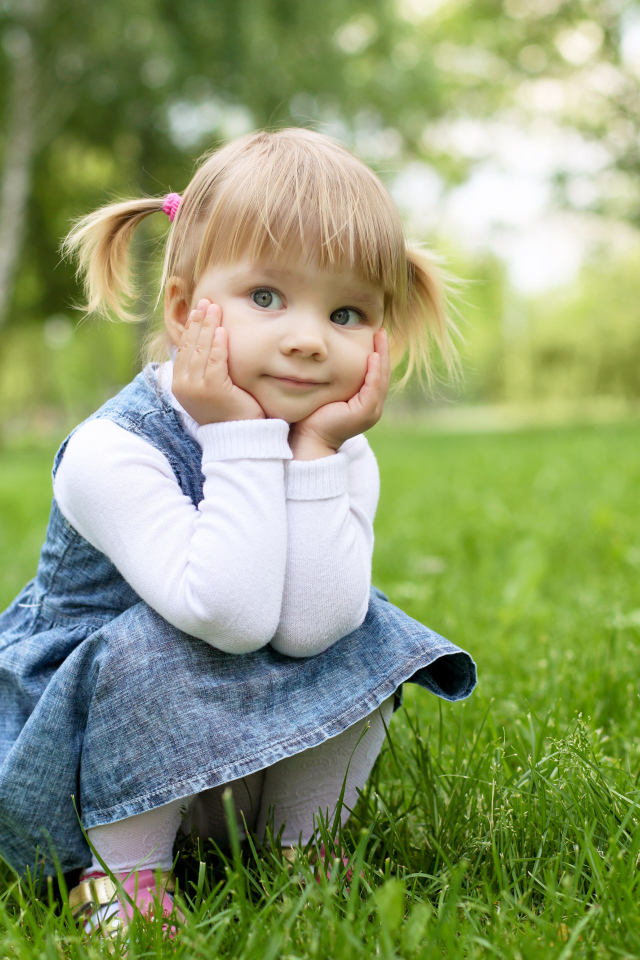 Маленькая девочка в сарафане сидит на траве 