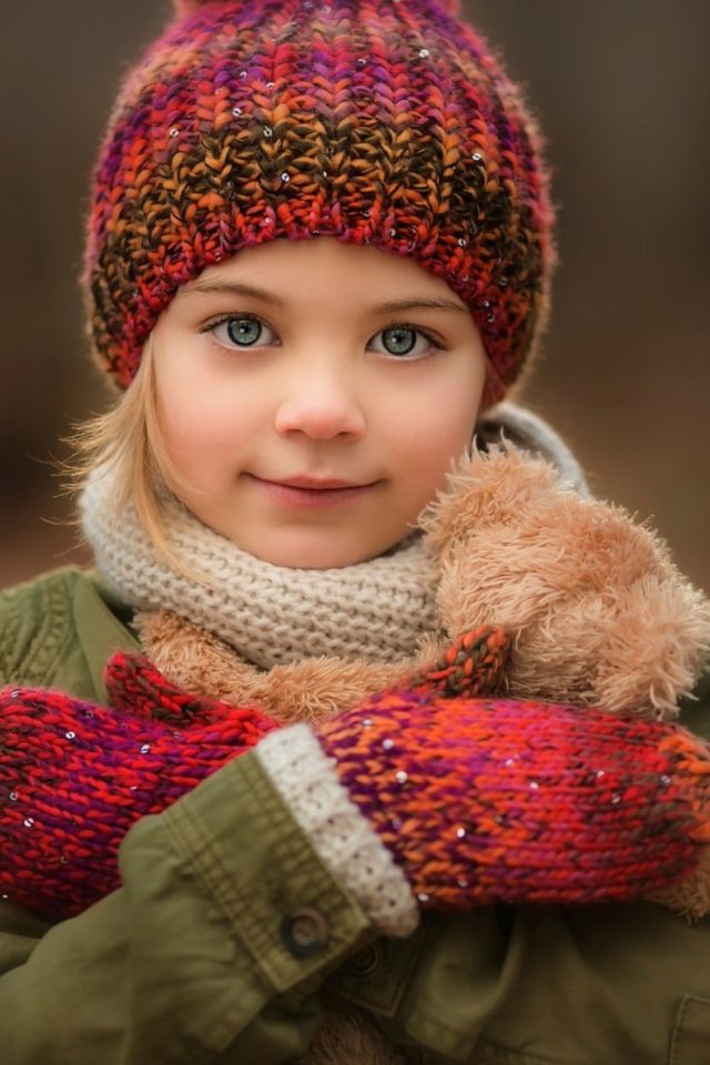 Маленькая девочка в теплой шапке и варежках  с игрушкой в руках 