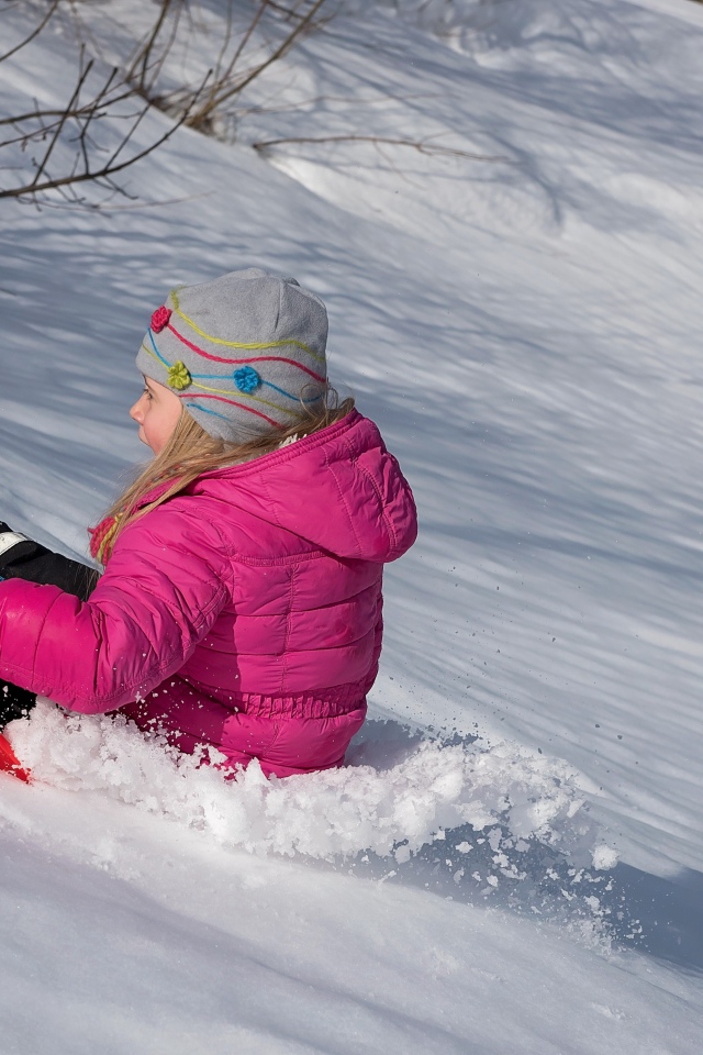 Маленькая девочка катится с заснеженной горки 
